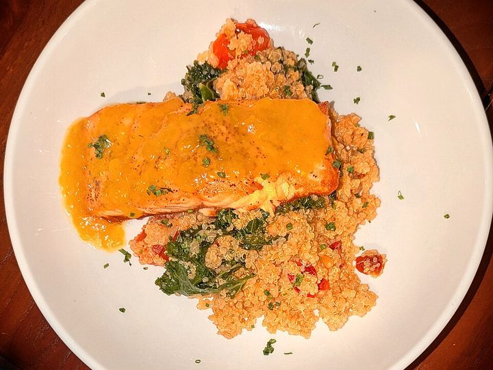 A plate of salmon on quinoa with kale and tomato